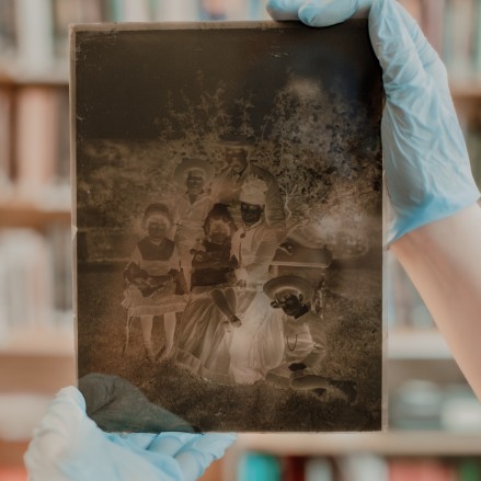 A librarian's gloved hands hold a glass plate negative image
