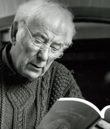 A black and white photo of Seamus Heaney reading from a paperback book