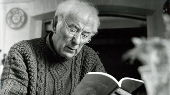 A black and white photo of Seamus Heaney reading from a paperback book