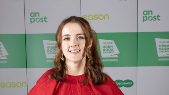 Picture of Molly Nic Céile in a red dress with an An Post Book Award in her hands. 