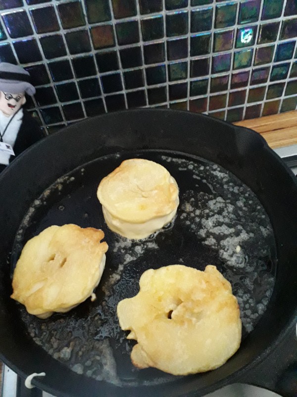 Apple fritters cooking in a frying pan