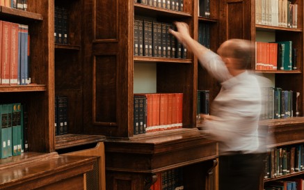 A blurred image of a man replacing a book on a shelf in the NLI Main Reading Room