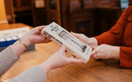 Close up photograph of two peoples hands showing an exchange of a book between a staff member with reader at Reading Room reception desk